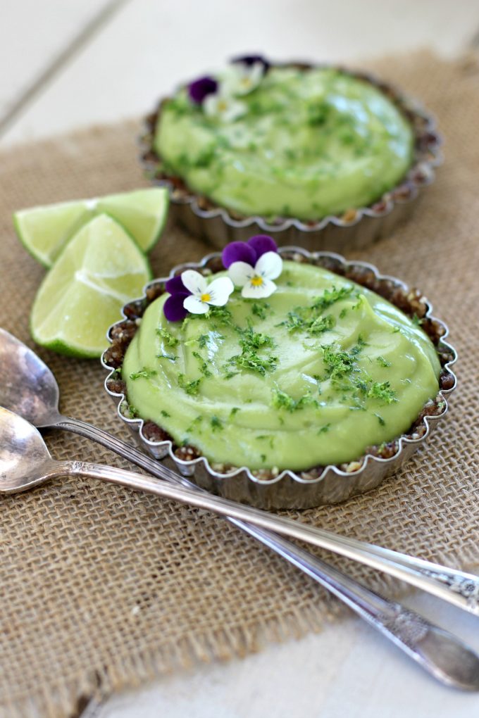 Two Raw Vegan Avocado Lime Tarts with spoons and lime wedges