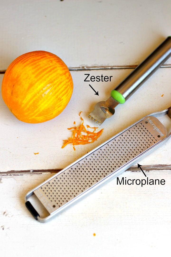 A zested orange on a white background with a zester tool and a microplane.