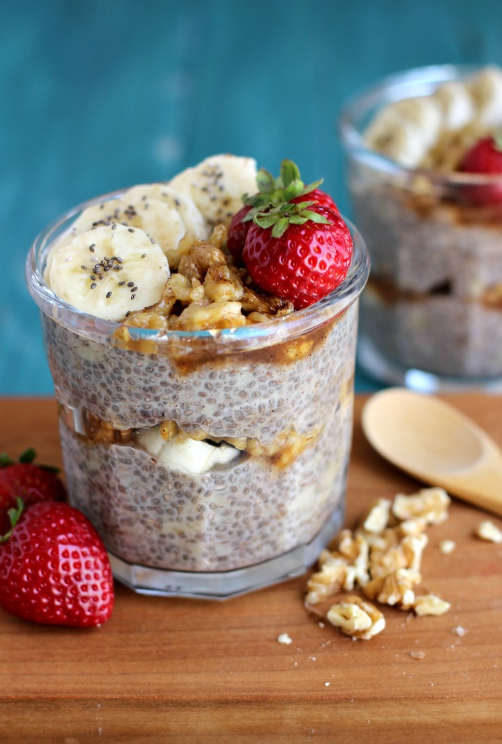 2 glass jars of chia pudding with a middle layer of banana slices and walnuts and another layer of chia pudding topped with banana slices, walnuts and strawberries.