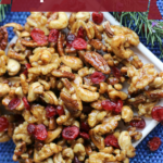 Pinterest graphic of a white plate on a royal blue background with mixed maple glazed nuts and dried cranberries