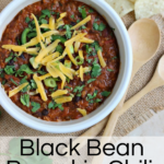 white bowl of black bean pumpkin chili topped with green onions, cilantro and shredded cheddar cheese