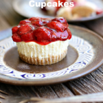 Pinterest graphic cheesecake cupcake with strawberry topping on a brown plate on a rustic background