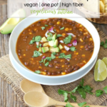 Pinterest graphic of a white bowl with black bean soup garnished with avocado chunks, cilantro and red onion on a rustic surface