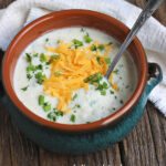 Pinterest graphic blue crock of potato soup with cheese and parsley on a rustic background