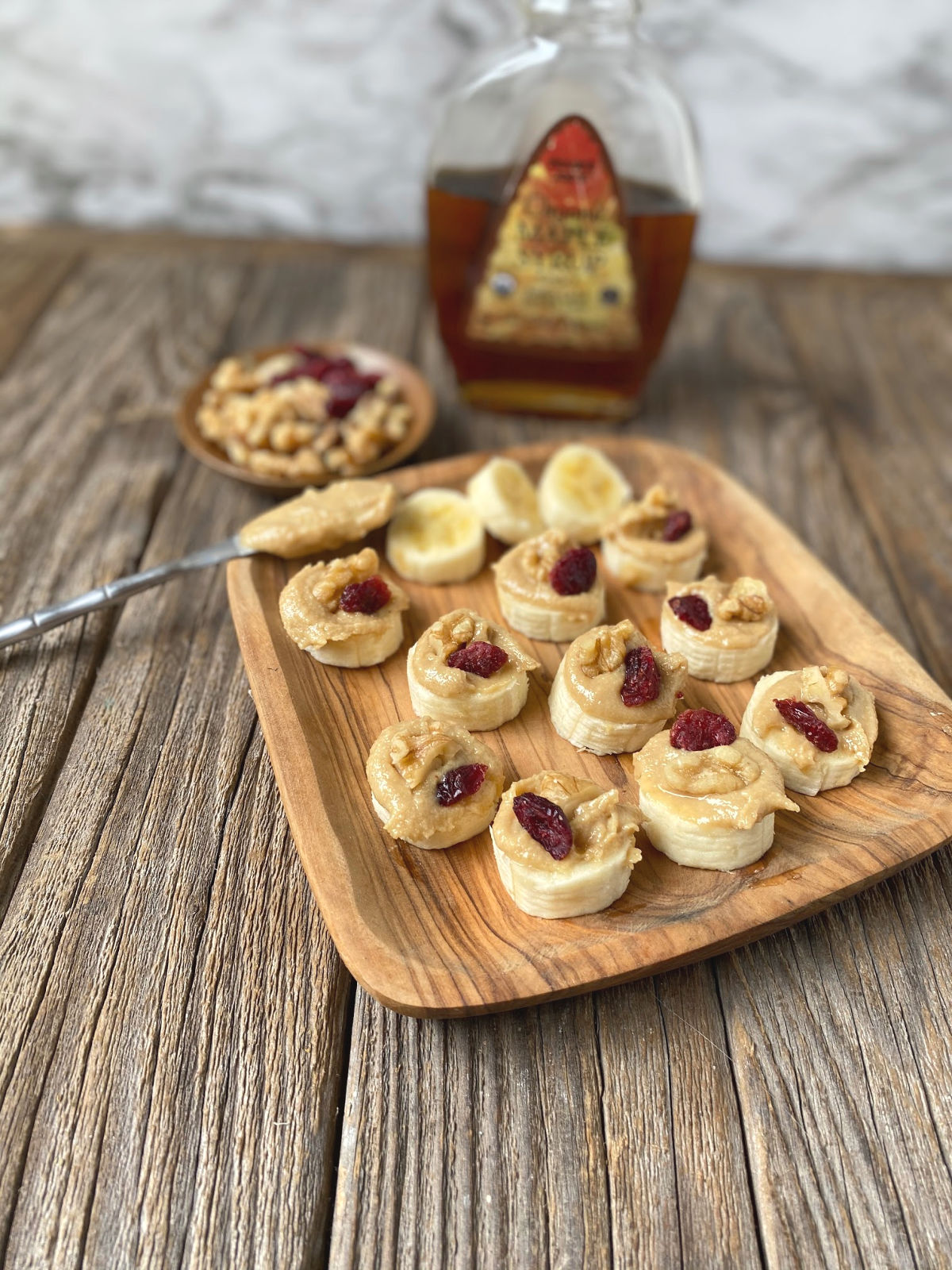 wooden plate of banana slices topped with tahini, walnut and dried cranberries